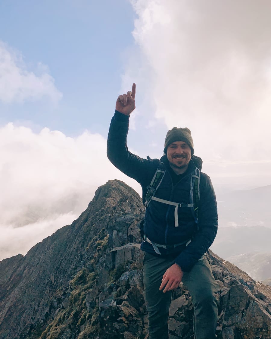 Carl on a ridgeline above the clouds, pointing skyward